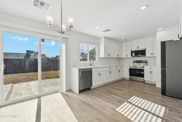 kitchen with hanging light fixtures, white cabinets, stainless steel appliances, and light hardwood / wood-style floors