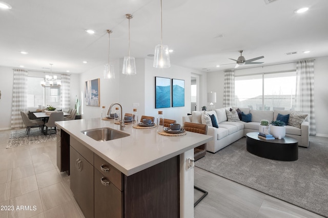 kitchen with ceiling fan with notable chandelier, decorative light fixtures, sink, a center island with sink, and dark brown cabinets