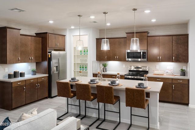 kitchen with dark brown cabinets, hanging light fixtures, appliances with stainless steel finishes, sink, and a center island with sink