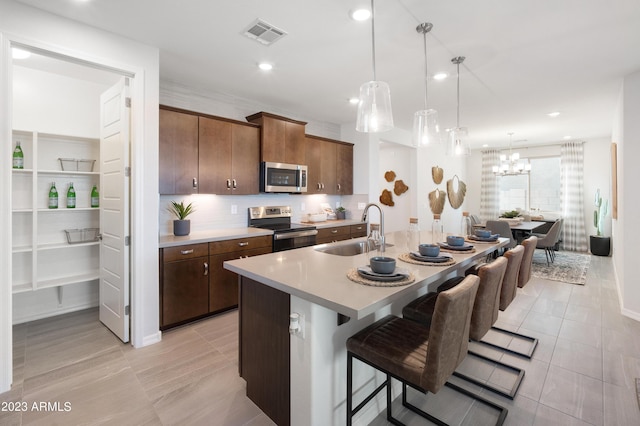 kitchen featuring hanging light fixtures, appliances with stainless steel finishes, sink, a kitchen bar, and an island with sink