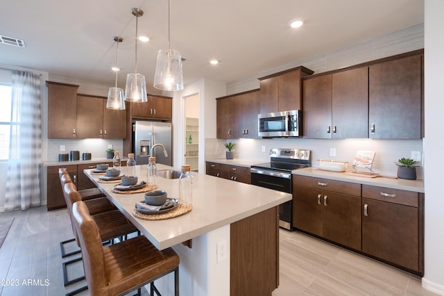 kitchen with hanging light fixtures, sink, dark brown cabinetry, stainless steel appliances, and a center island with sink