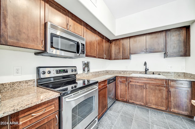 kitchen with light tile patterned floors, light stone countertops, appliances with stainless steel finishes, and sink