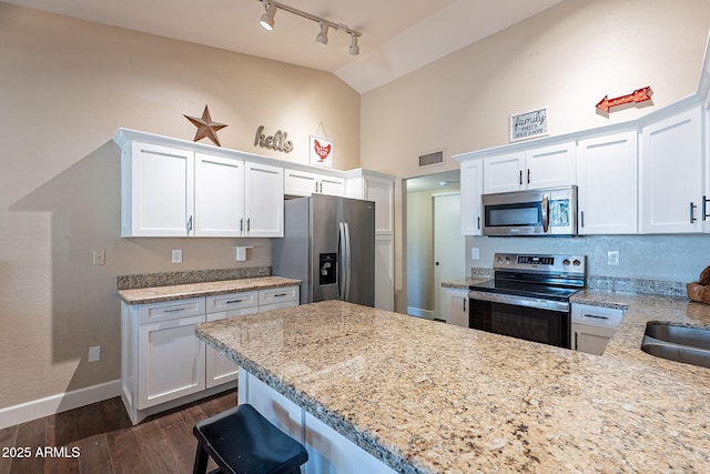 kitchen featuring dark wood-type flooring, white cabinetry, stainless steel appliances, light stone counters, and a kitchen bar