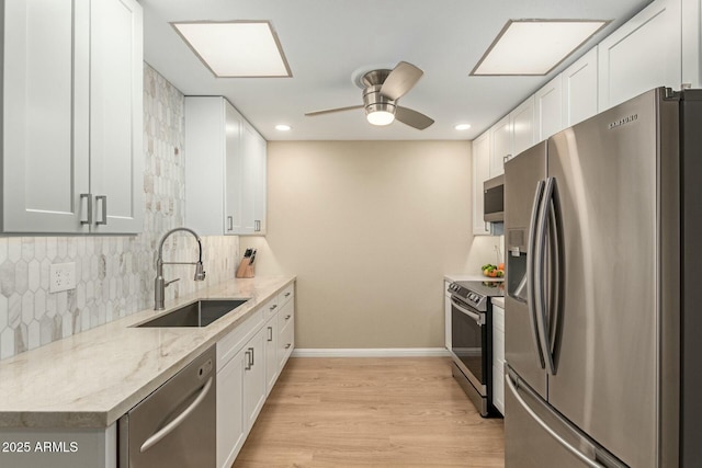 kitchen featuring tasteful backsplash, light wood-style flooring, appliances with stainless steel finishes, white cabinets, and a sink