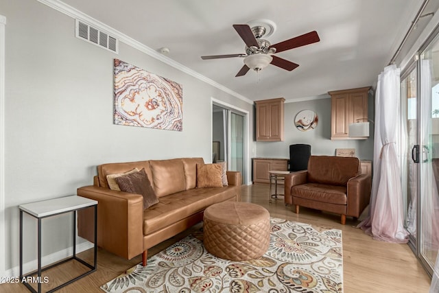 living room with ornamental molding, visible vents, light wood-style flooring, and a ceiling fan