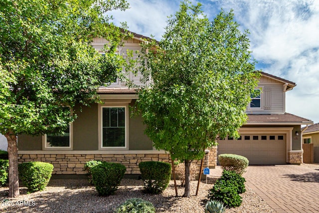 14727 W Pasadena Ave, Litchfield Park, AZ 85340 - view of property hidden behind natural elements with stone siding, an attached garage, decorative driveway, and stucco siding