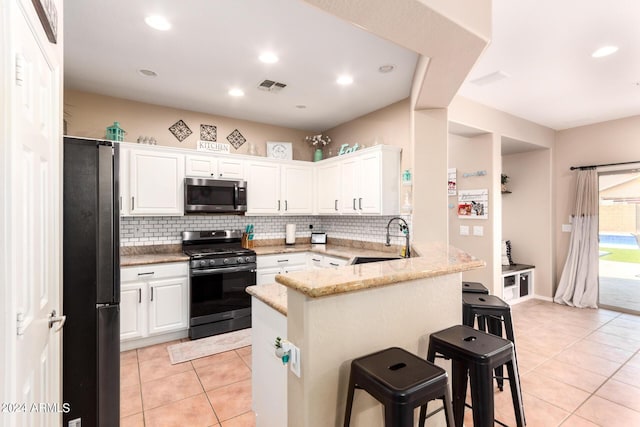 kitchen featuring white cabinets, sink, appliances with stainless steel finishes, a kitchen bar, and kitchen peninsula