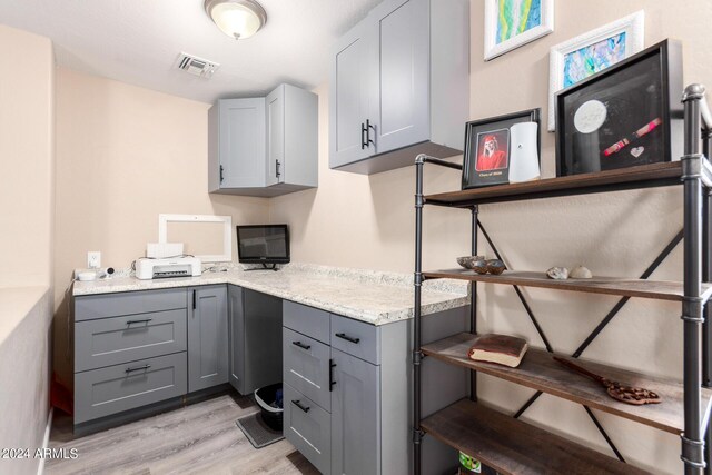 kitchen featuring gray cabinets, light stone countertops, and light wood-type flooring