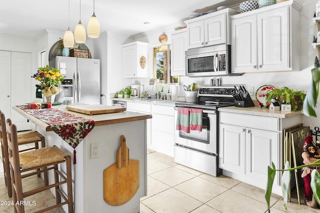 kitchen featuring pendant lighting, sink, light tile patterned floors, white cabinetry, and stainless steel appliances