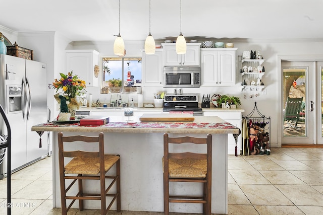 kitchen featuring white cabinets, appliances with stainless steel finishes, hanging light fixtures, and a breakfast bar area