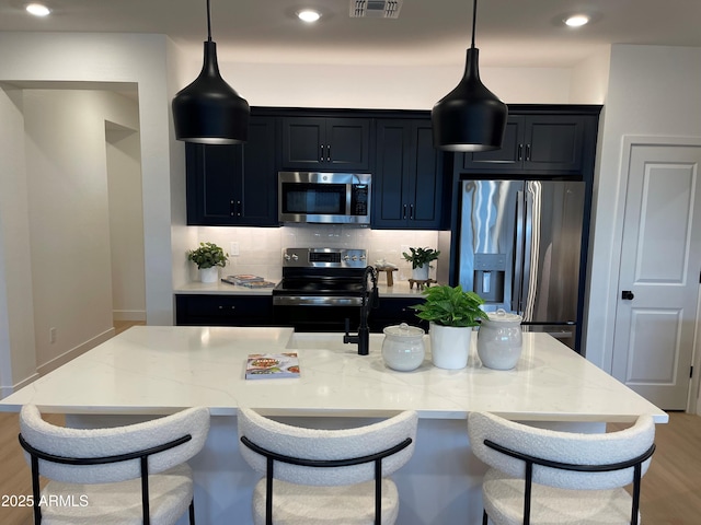 kitchen featuring light stone counters, decorative light fixtures, a center island with sink, and appliances with stainless steel finishes