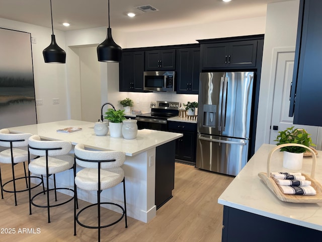 9965 W Flower St, Avondale, AZ 85392 - kitchen with decorative light fixtures, a center island with sink, appliances with stainless steel finishes, a kitchen breakfast bar, and light stone countertops