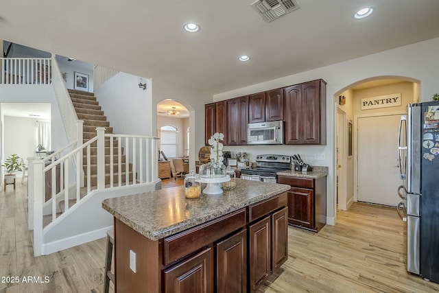 kitchen with appliances with stainless steel finishes, light hardwood / wood-style flooring, dark brown cabinetry, and a center island