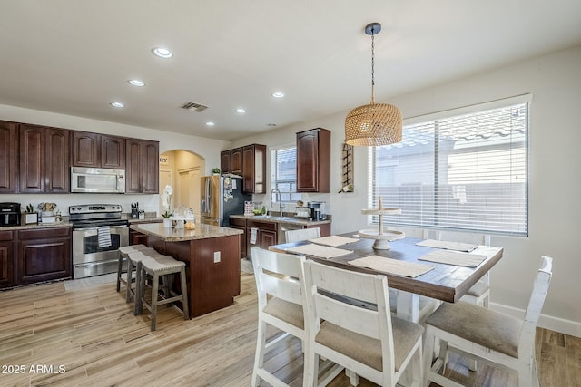 kitchen with dark brown cabinetry, appliances with stainless steel finishes, pendant lighting, and a kitchen island