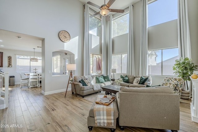 living room featuring light wood-type flooring, ceiling fan, and a high ceiling