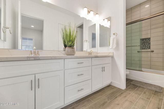 bathroom with toilet, double vanity, enclosed tub / shower combo, and wood finish floors