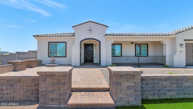 mediterranean / spanish-style home featuring a porch, a ceiling fan, a tile roof, and stucco siding