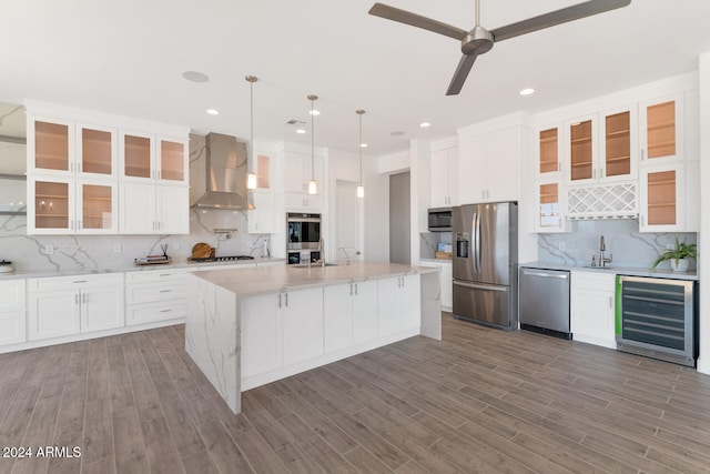 kitchen featuring beverage cooler, wood finished floors, white cabinets, appliances with stainless steel finishes, and wall chimney range hood