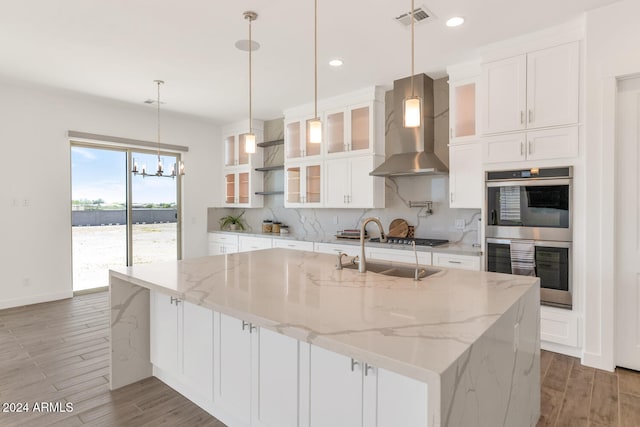 kitchen featuring light wood-style flooring, stainless steel appliances, visible vents, backsplash, and wall chimney exhaust hood