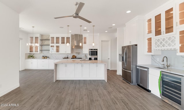 kitchen with wine cooler, stainless steel appliances, a sink, light countertops, and wall chimney exhaust hood