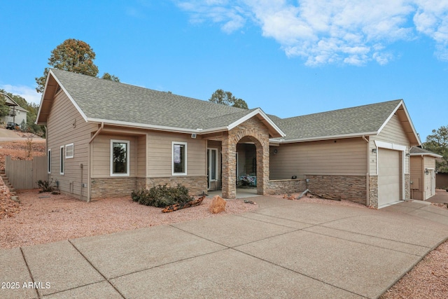 view of front facade featuring stone siding, roof with shingles, an attached garage, and concrete driveway