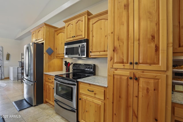 kitchen featuring light stone countertops, light tile patterned floors, appliances with stainless steel finishes, and vaulted ceiling