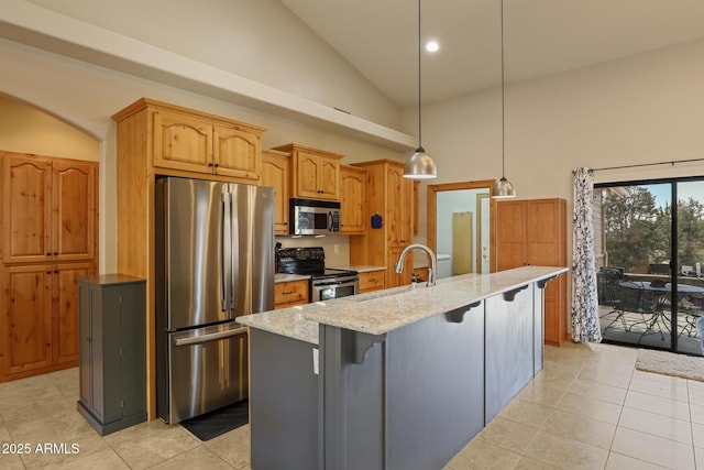 kitchen featuring light stone counters, stainless steel appliances, hanging light fixtures, a kitchen island with sink, and a sink