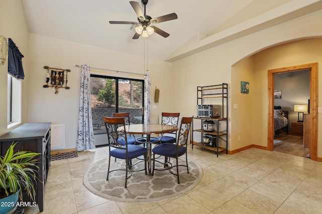 dining room featuring arched walkways, ceiling fan, light tile patterned floors, lofted ceiling, and baseboards