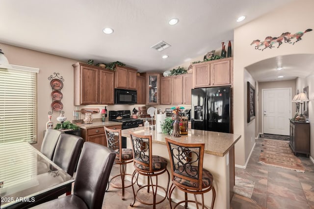 kitchen with a breakfast bar, lofted ceiling, black appliances, light stone countertops, and a center island with sink