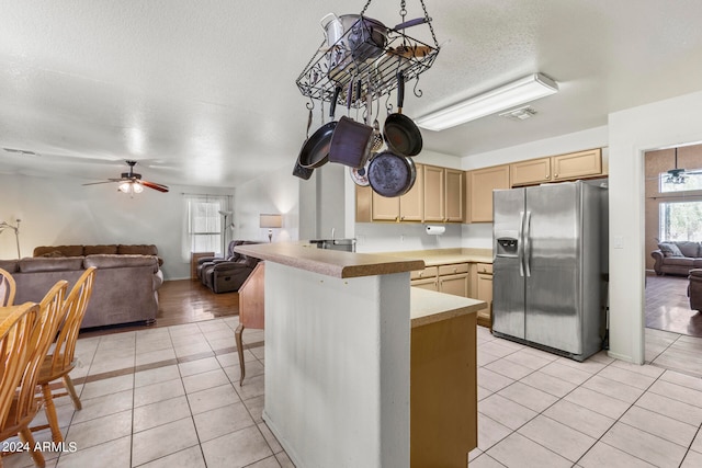 kitchen featuring kitchen peninsula, light brown cabinetry, light tile patterned floors, stainless steel fridge with ice dispenser, and a breakfast bar area