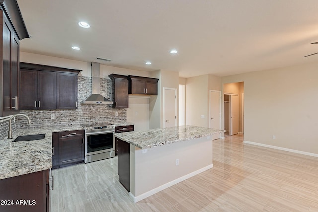 kitchen featuring wall chimney range hood, sink, electric stove, a center island, and light stone counters