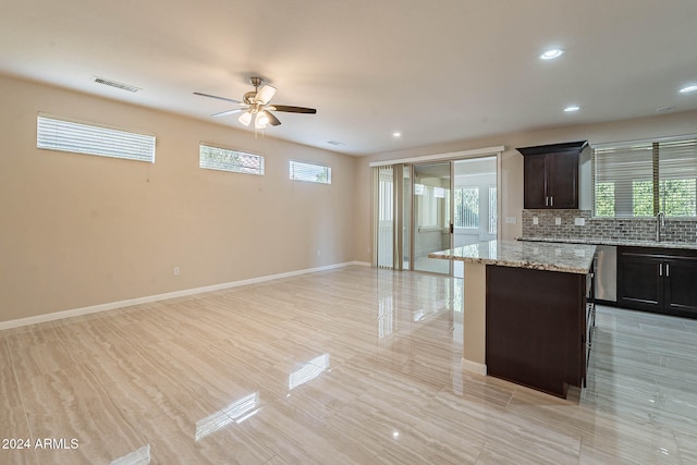 kitchen featuring ceiling fan, backsplash, light stone countertops, sink, and a center island