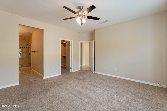 unfurnished bedroom with connected bathroom, ceiling fan, light colored carpet, and a walk in closet