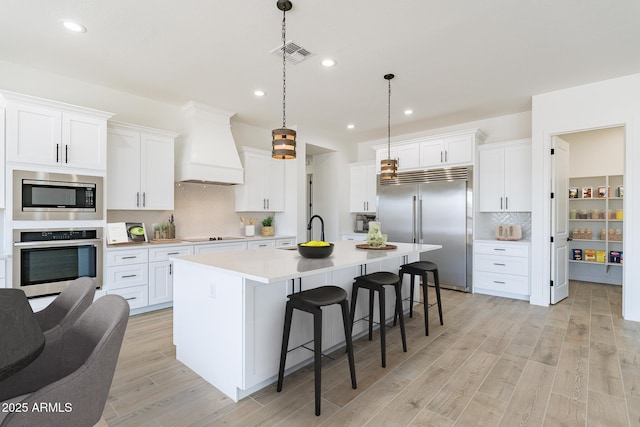 kitchen with built in appliances, premium range hood, visible vents, light countertops, and hanging light fixtures