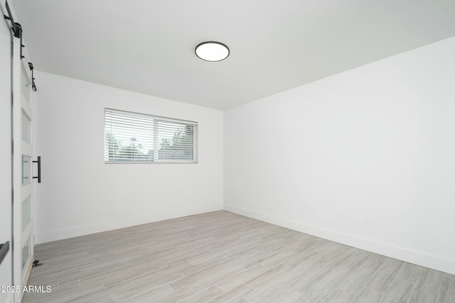 unfurnished room with baseboards, light wood finished floors, and a barn door