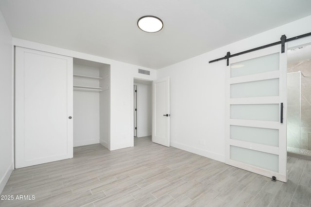 unfurnished bedroom with a barn door, baseboards, visible vents, wood finish floors, and a closet