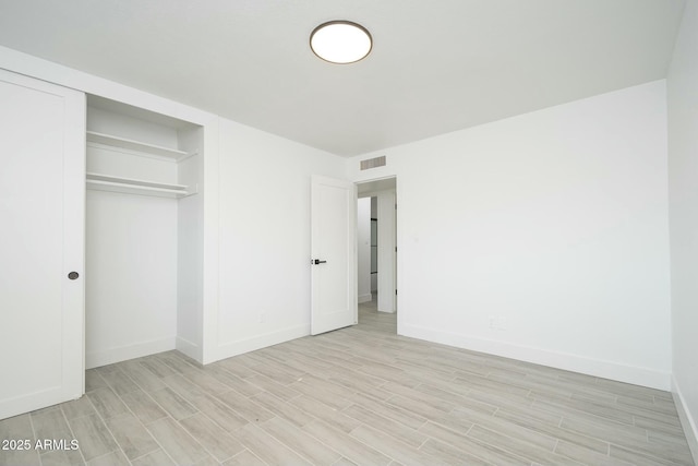 unfurnished bedroom featuring light wood-style floors, baseboards, visible vents, and a closet