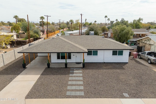 single story home featuring concrete driveway, an attached carport, a shingled roof, and fence