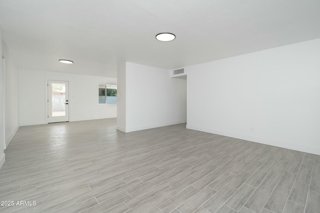 empty room with light wood-type flooring, visible vents, and baseboards