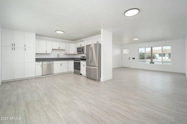 kitchen featuring stainless steel appliances, white cabinetry, open floor plan, light wood finished floors, and dark countertops