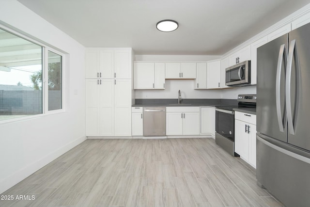 kitchen with dark countertops, white cabinetry, appliances with stainless steel finishes, and a sink