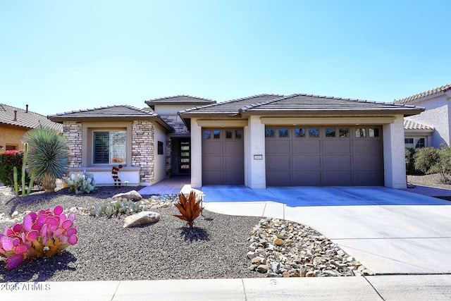 prairie-style home featuring an attached garage, a tile roof, stucco siding, stone siding, and driveway