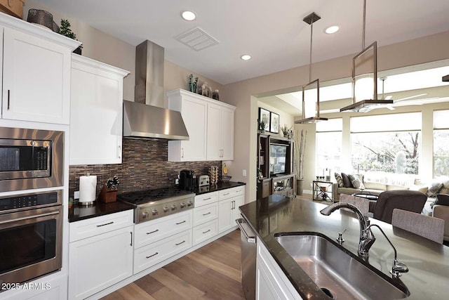 kitchen featuring visible vents, a sink, appliances with stainless steel finishes, wall chimney range hood, and tasteful backsplash