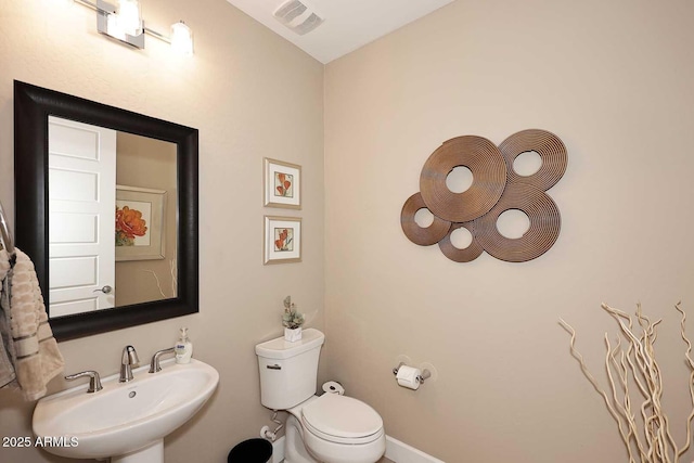 half bath with a sink, visible vents, baseboards, and toilet