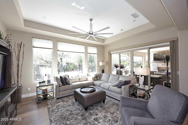 living room with a tray ceiling, visible vents, wood finished floors, and a ceiling fan