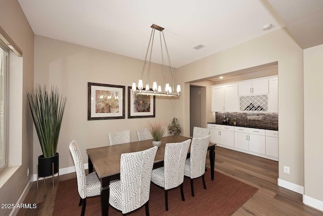 dining room with dark wood-style floors, visible vents, a chandelier, and baseboards