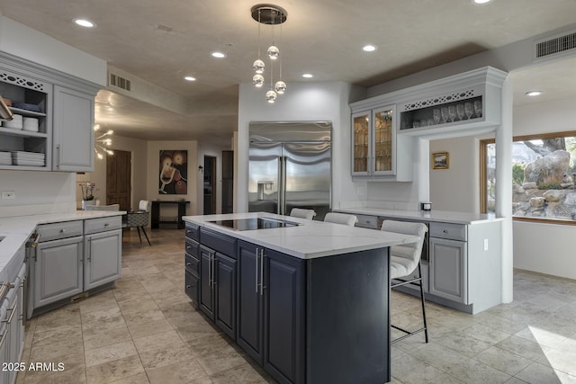 kitchen featuring gray cabinets, pendant lighting, an island with sink, stainless steel built in fridge, and light stone countertops