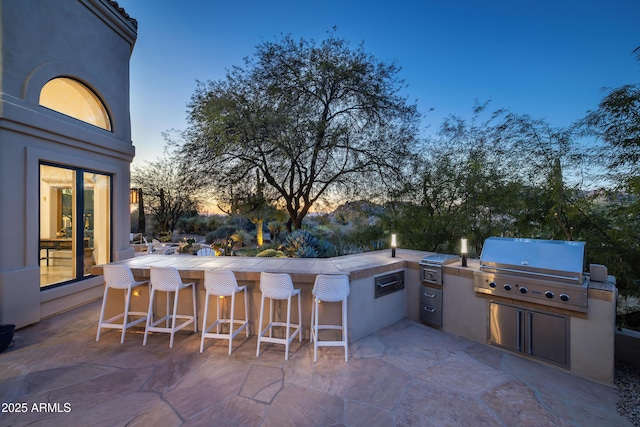 patio terrace at dusk featuring a grill and exterior bar