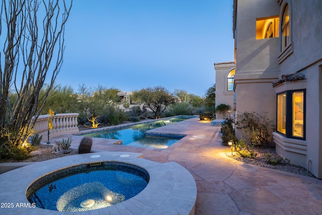 pool at dusk featuring an in ground hot tub and a patio