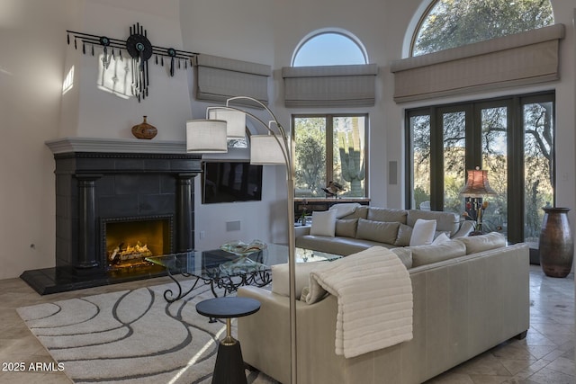 living room with a tiled fireplace, plenty of natural light, and a towering ceiling